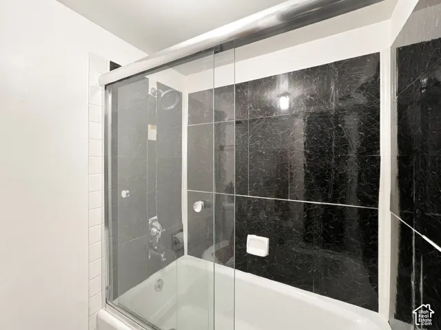 Built-in bathtub with shower, black marbled wall tiling, white subway tile accents, and sliding glass shower door