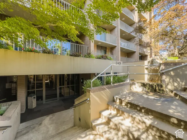 Multi-story building exterior with individual balconies, metal balcony railings, and an entry with glass doors
