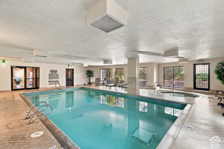 Indoor swimming pool with an integrated hot tub and perimeter tile detailing, surrounded by tiled decking