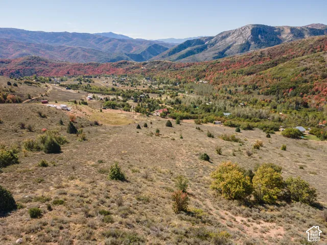 Expansive mountainous landscape with natural terrain, distant structures, and diverse tree coverage