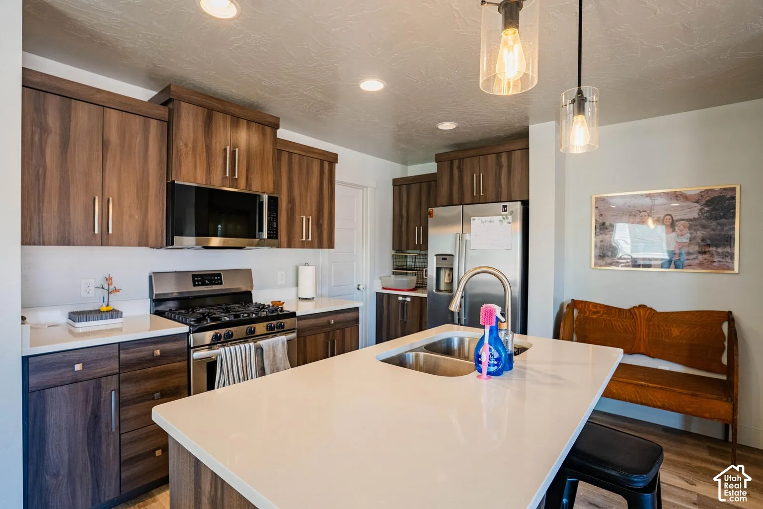 Kitchen featuring wood-finish cabinetry, stainless steel appliances, a center island with sink, quartz countertops, and recessed lighting