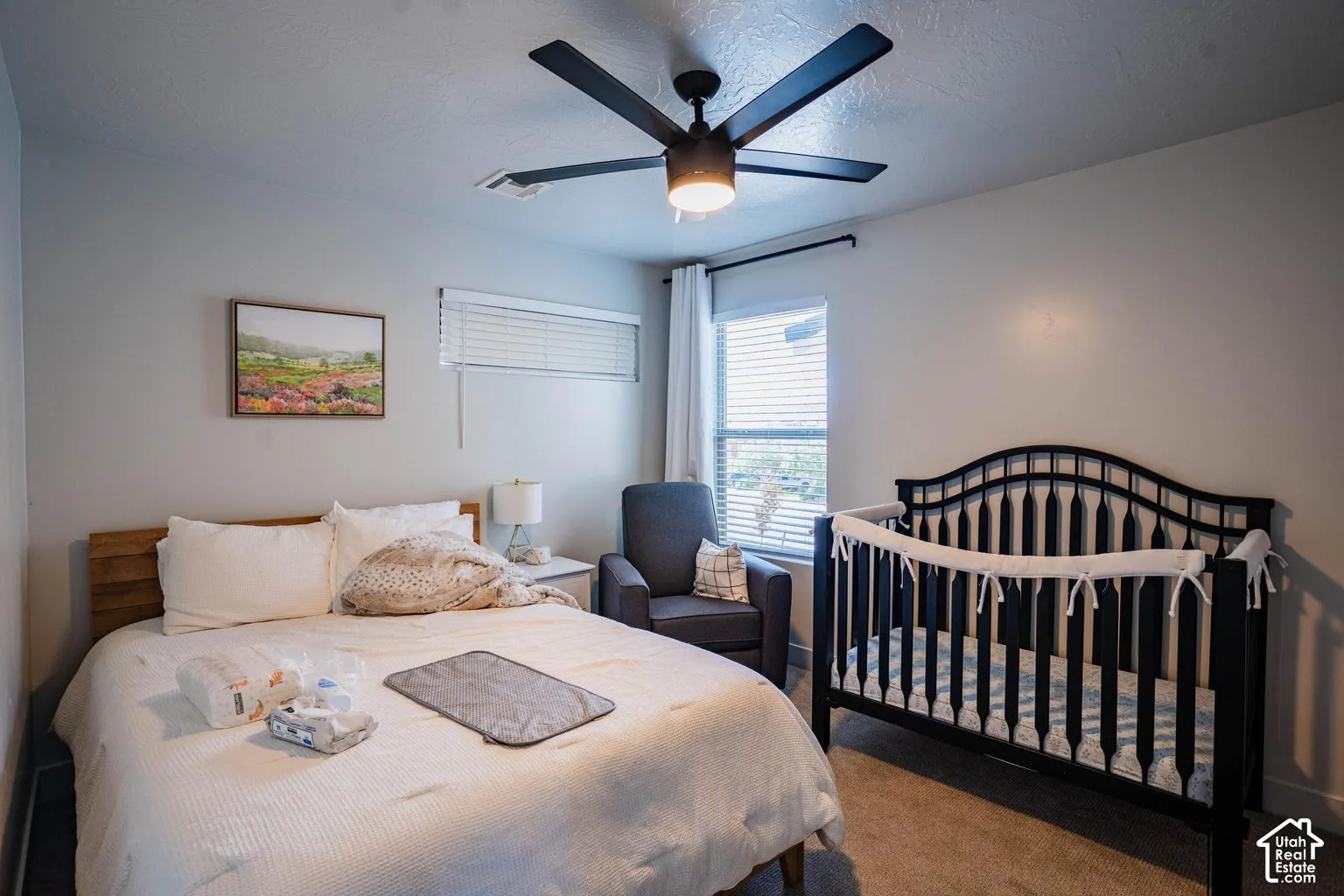 Neutral wall color, ceiling fan with integrated lighting, wood-finish headboard, window with blinds, and carpeting