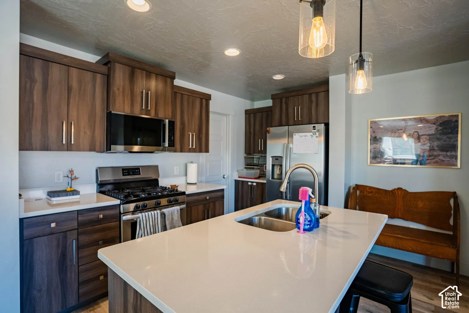 Kitchen featuring wood-finish cabinetry, stainless steel appliances, a center island with an undermount double-bowl sink, and recessed lighting
