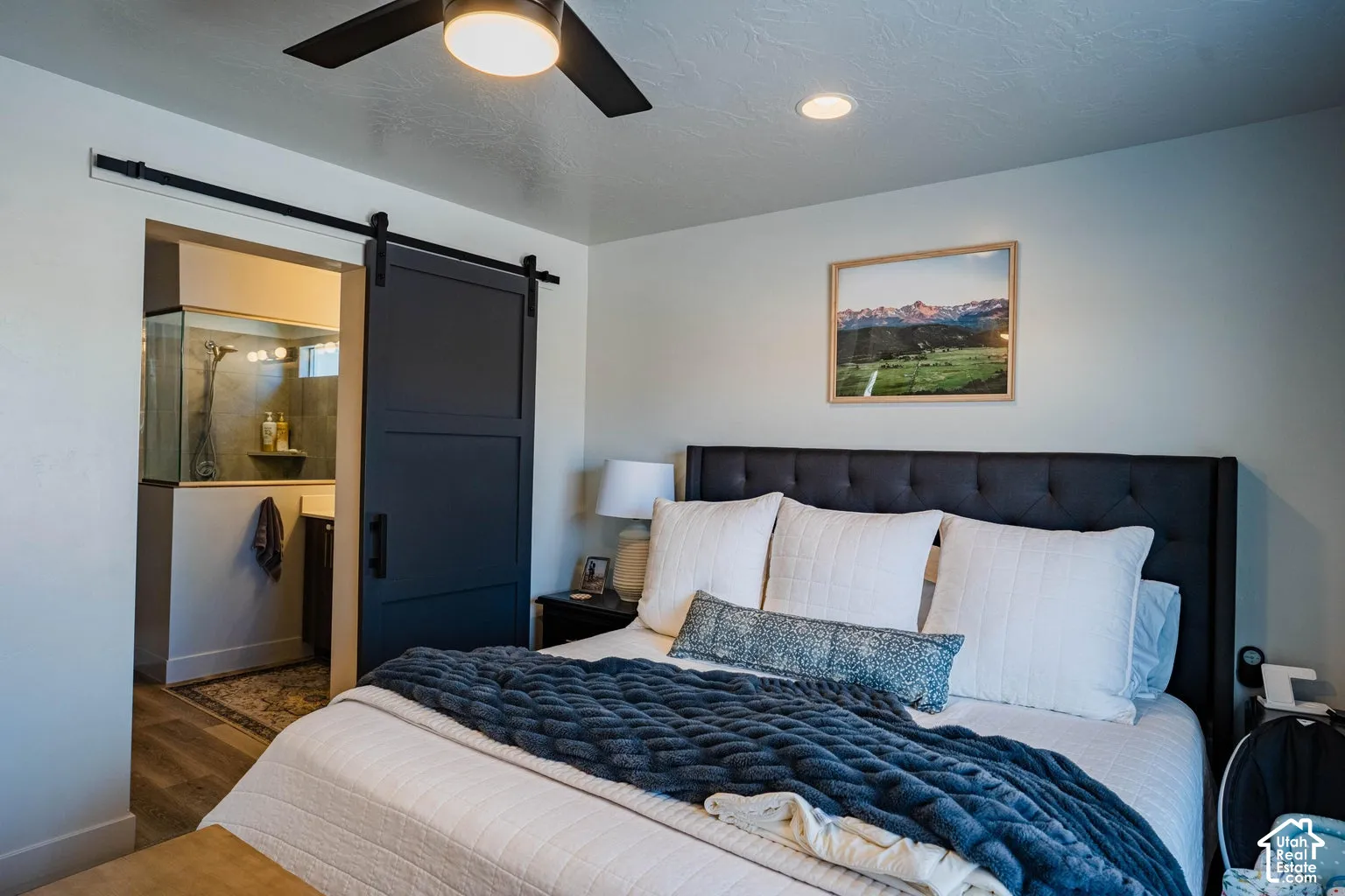 Recessed ceiling lighting, a dark wood-finish barn door, and a ceiling fan with integrated lighting