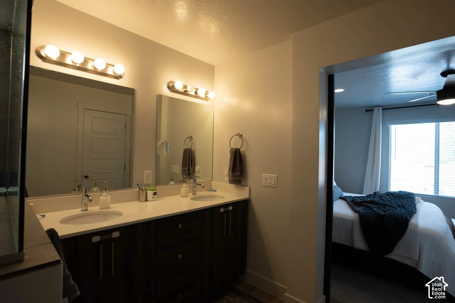 Double vanity with ample counter space, dual undermount sinks, wall-mounted light fixtures, and dark wood-finish cabinetry