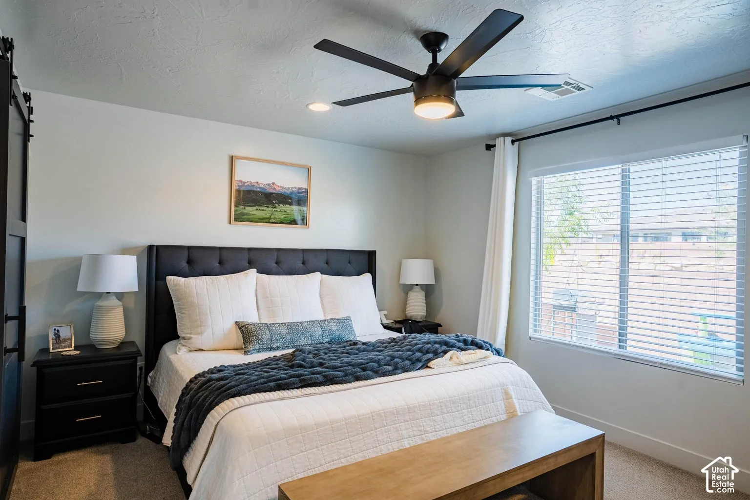Spacious room featuring a large window with blinds, ceiling fan with integrated lighting, and a dark upholstered headboard