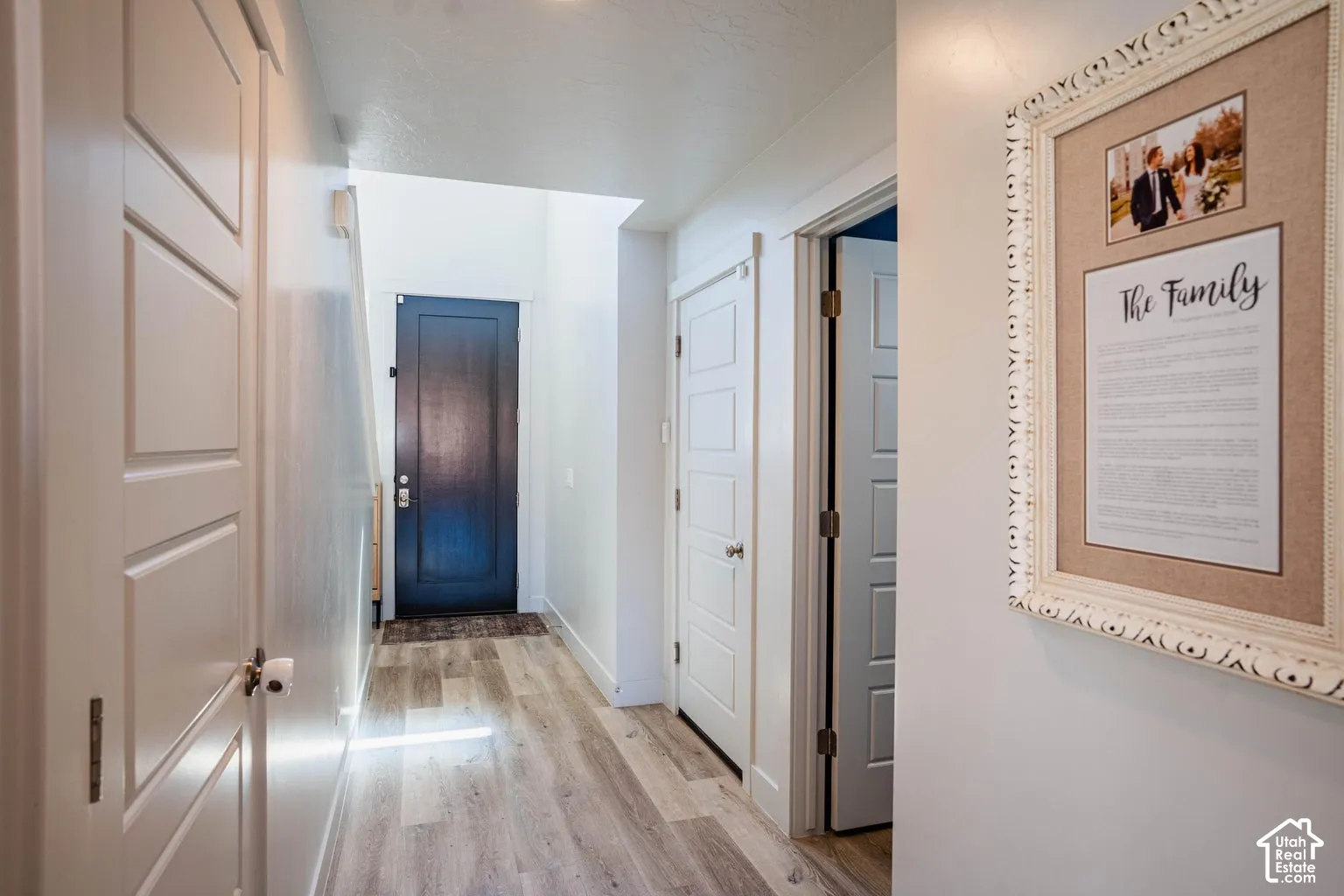 Hallway featuring light wood-finish flooring, white paneled doors, and a dark paneled door