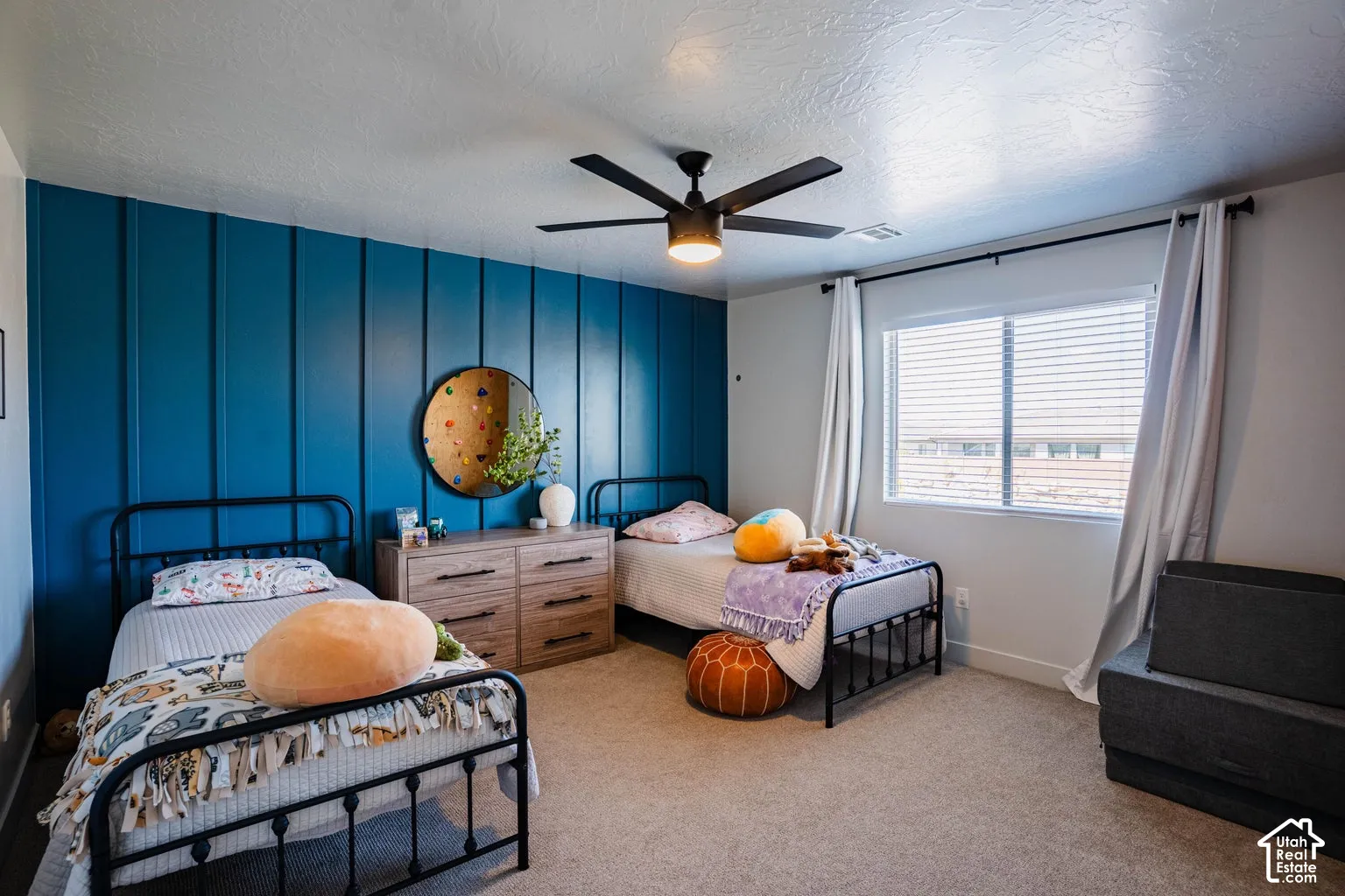 Recessed window with blinds, blue accent wall with vertical paneling, light-colored carpeting, ceiling fan with integrated lighting, and a neutral wall color