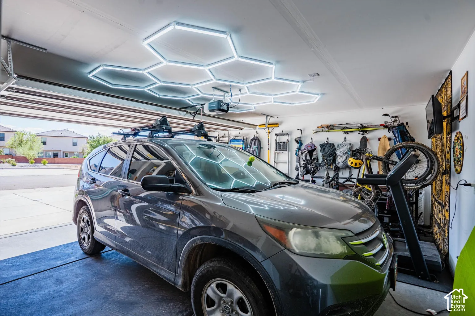 Garage featuring hexagonal overhead lighting, a mounted wall television, a garage door, and ample storage space