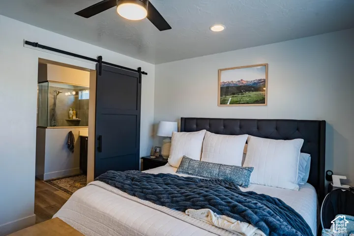 Recessed ceiling lighting, a dark wood-finish barn door, and a ceiling fan with integrated lighting