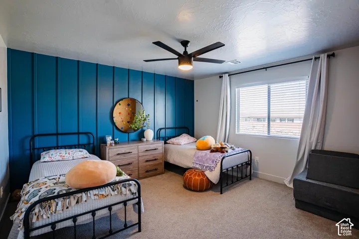 Recessed window with blinds, blue accent wall with vertical paneling, light-colored carpeting, ceiling fan with integrated lighting, and a neutral wall color