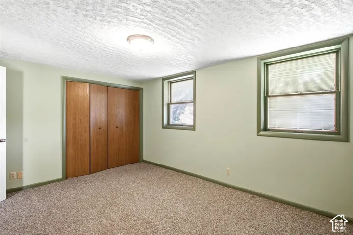 Two windows with blinds, wood-finish bi-fold closet doors, wall-mounted light fixture, and textured ceiling