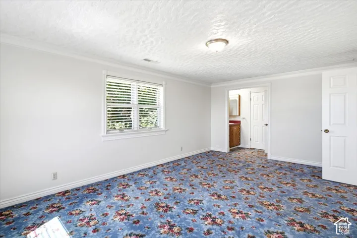 Room featuring patterned carpet, white walls, and crown molding