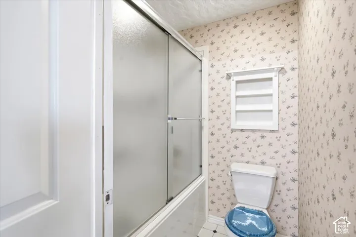 Bathroom featuring frosted glass sliding shower enclosure with chrome hardware, decorative tile walls, a porcelain toilet, and a louvered ventilation window