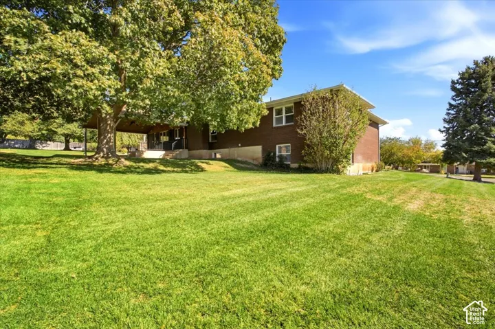 Expansive lawn with mature trees, a covered patio, and a brick exterior