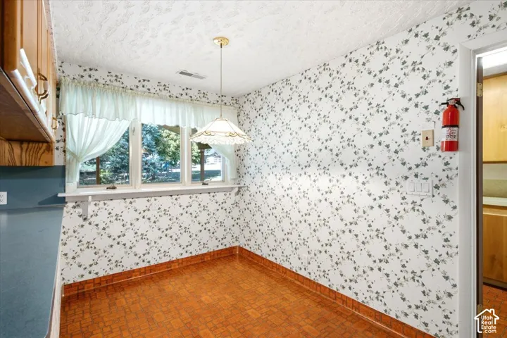 Wood cabinetry with brass-finish hardware, three-panel window, patterned wall covering, patterned flooring, and a ceiling-mounted light fixture