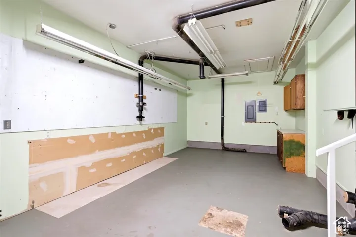 Utility room with fluorescent lighting, light green walls, wood-finish cabinetry, and a concrete floor