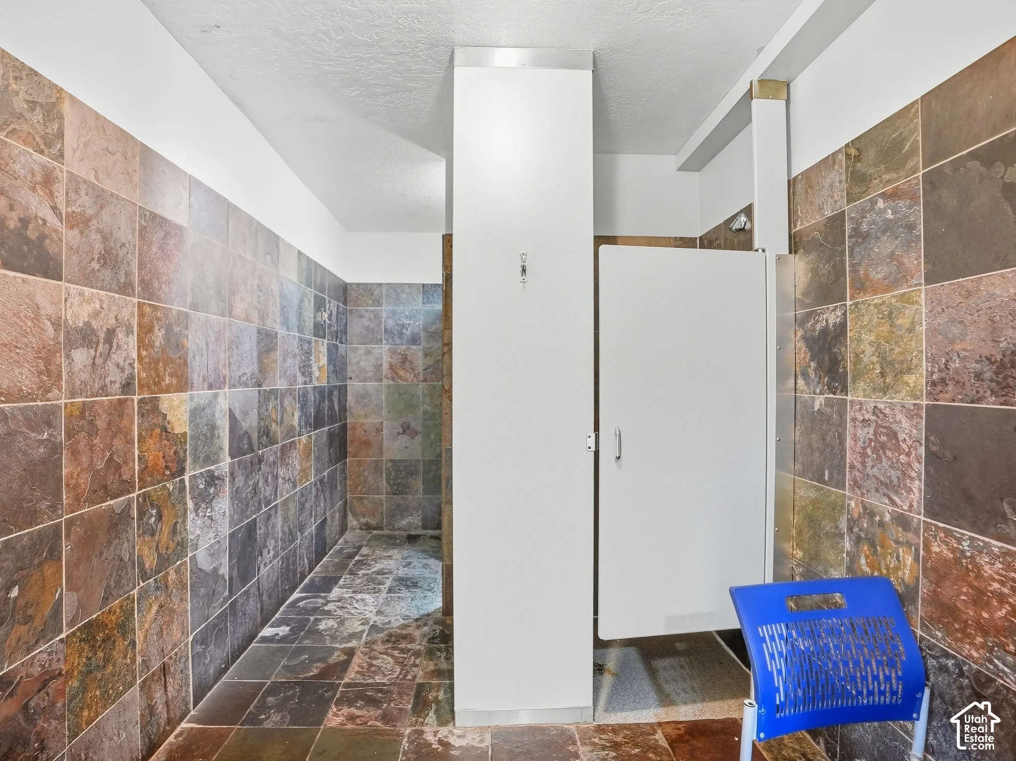 Full-height slate-style tile walls and flooring, with a private shower stall featuring a white door