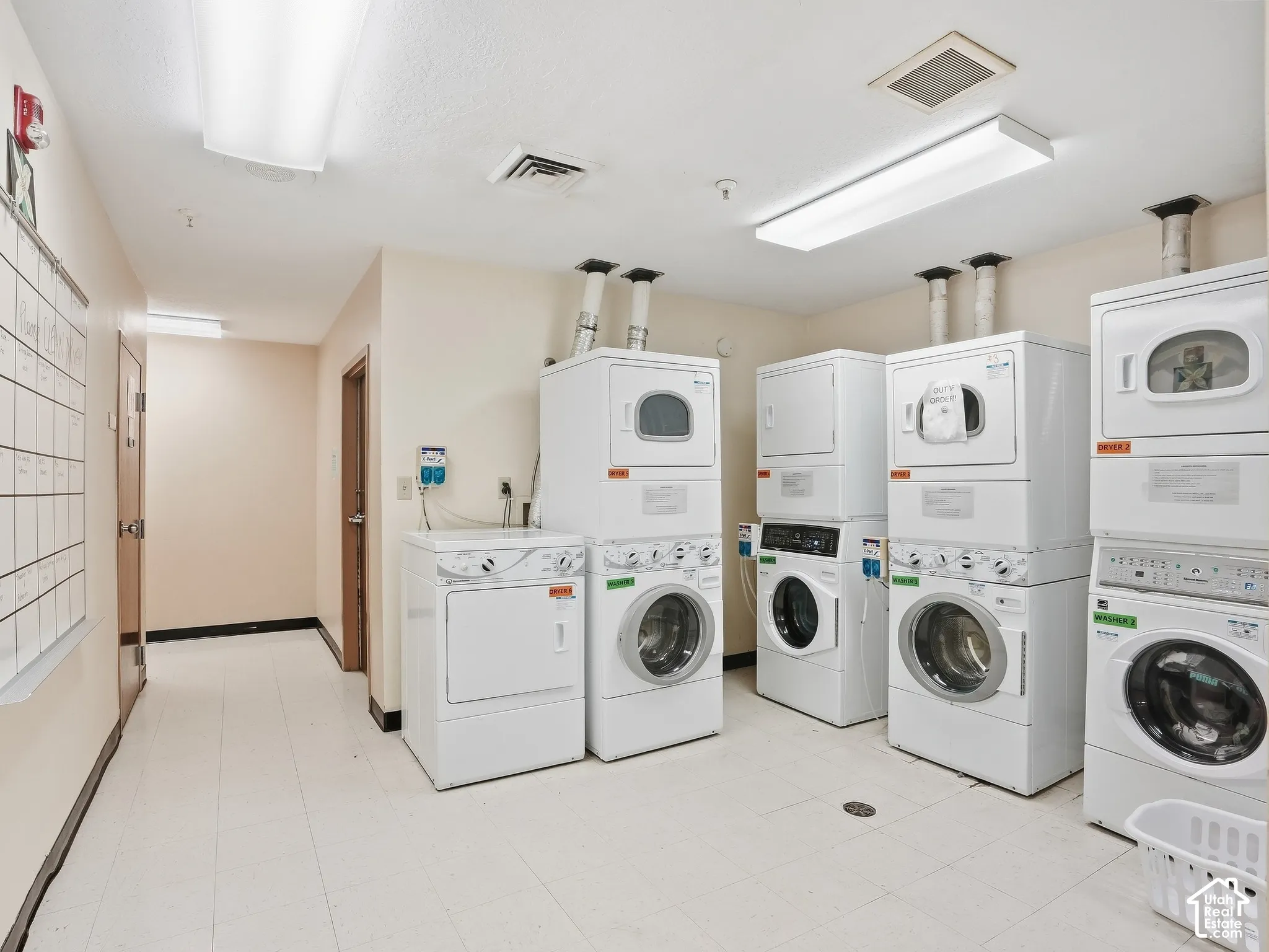 Multiple front-loading washing machines and top-loading dryers, ample overhead lighting, light-toned walls, and durable flooring
