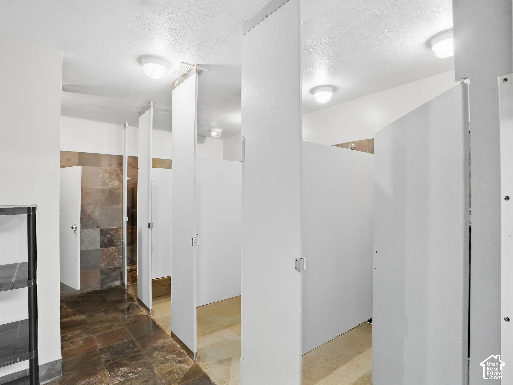 Multiple shower stalls featuring privacy partitions, tile flooring, and flush-mount ceiling lighting