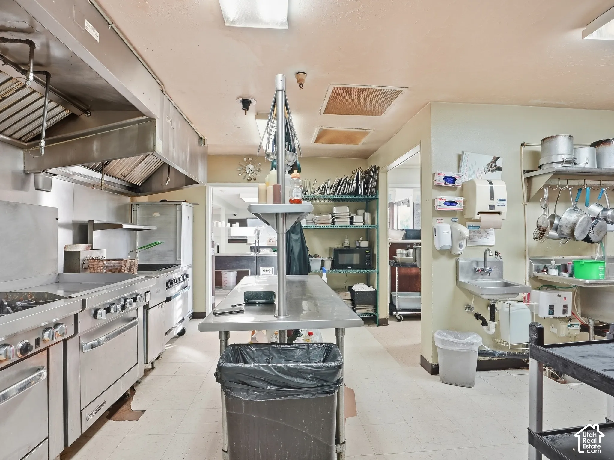 Stainless steel commercial kitchen with multiple ranges, deep fryer, and industrial hood system