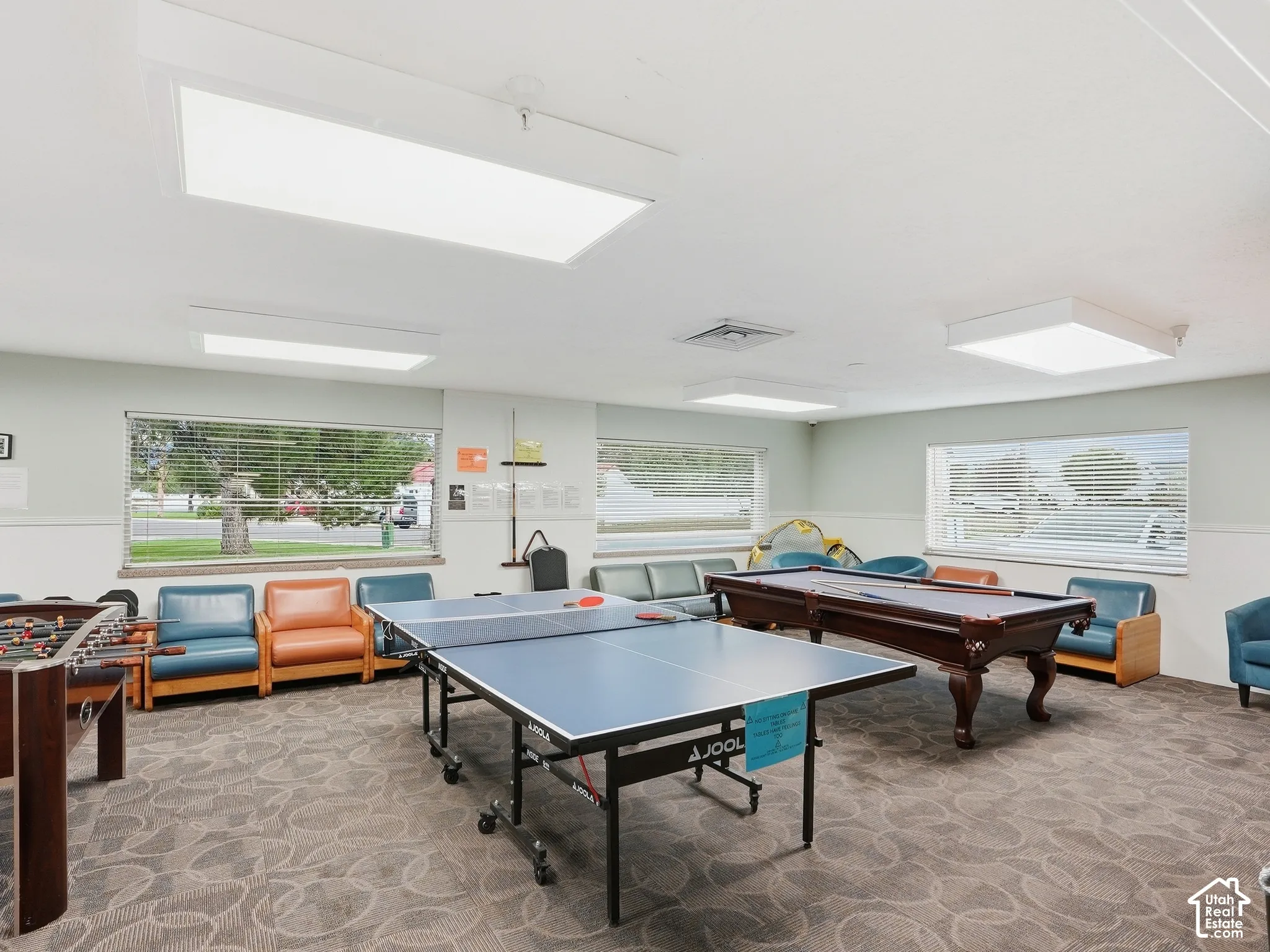 Recessed panel lighting illuminates a room with multiple windows, patterned carpeting, and a built-in shelf