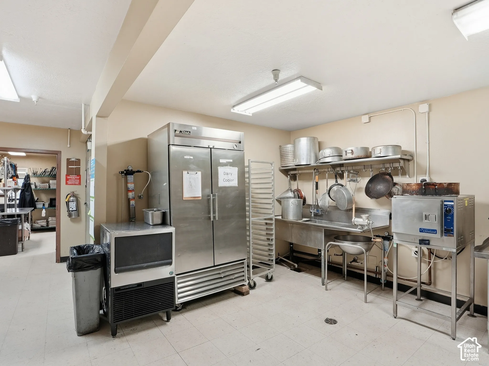 Commercial kitchen featuring stainless steel appliances, stainless steel sink, tile flooring, and fluorescent lighting