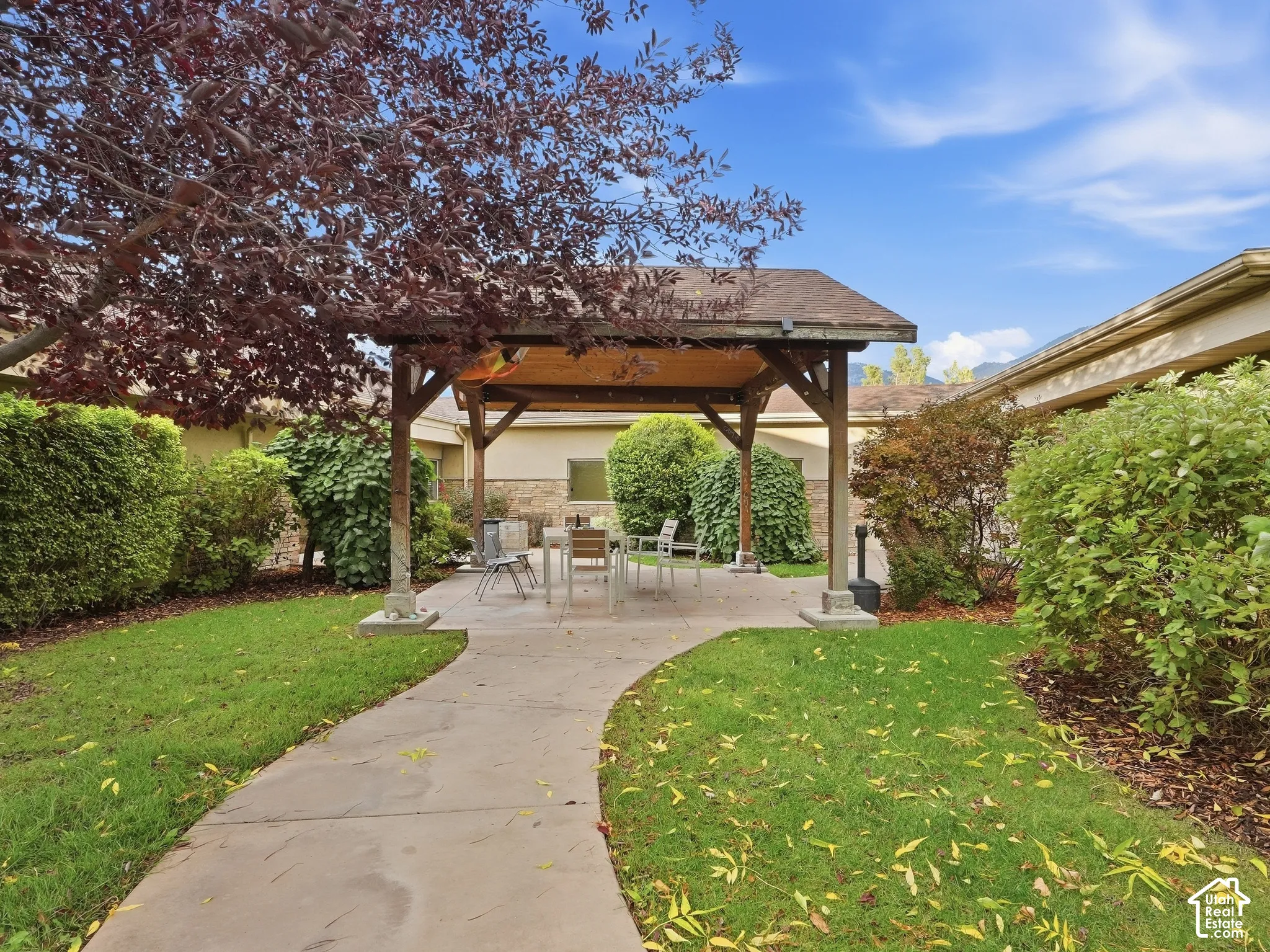 Outdoor living area with a covered patio, concrete pathway, manicured lawn, and mature landscaping