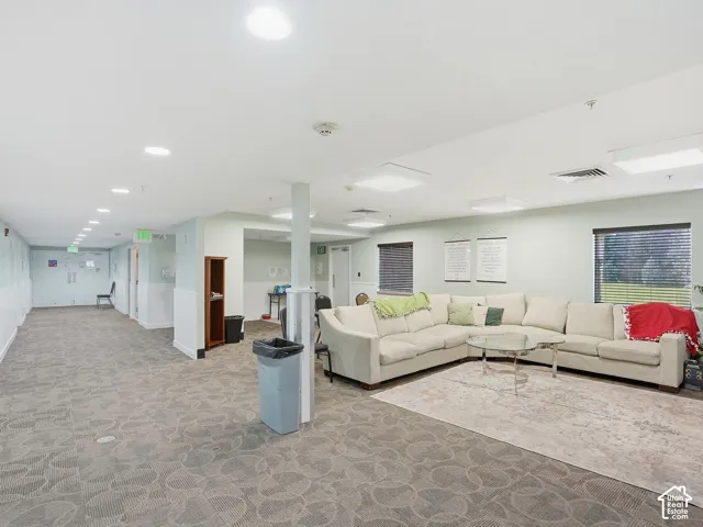 Carpeted flooring throughout, recessed ceiling lighting, and multiple windows with horizontal blinds