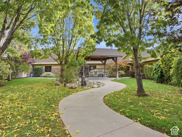 Manicured lawn with mature trees, stone-finish exterior, covered patio, and a winding pathway