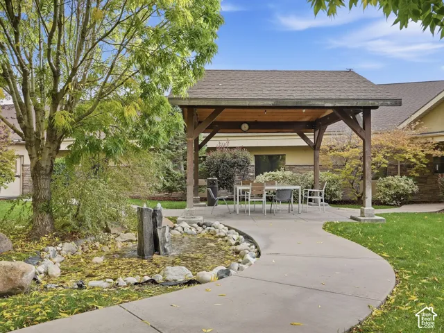 Covered patio structure with a concrete pad, a rock-lined pond with a water feature, and a paved walkway
