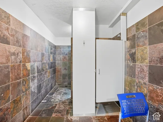 Full-height slate-style tile walls and flooring, with a private shower stall featuring a white door