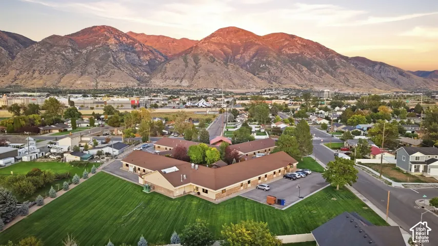 Expansive green space and a prominent building with a brown roof, situated in a developed area, with a distinct mountainous backdrop
