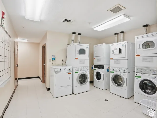Multiple front-loading washing machines and top-loading dryers, ample overhead lighting, light-toned walls, and durable flooring