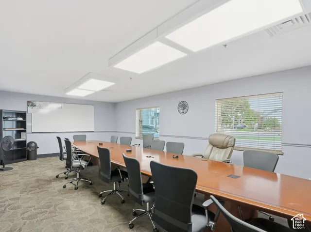 Spacious meeting room featuring a large wood-finish conference table, recessed ceiling lighting, textured carpet, and neutral wall tones