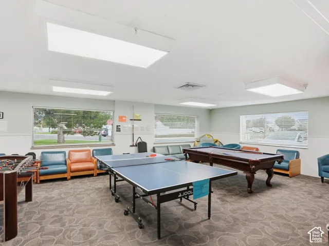 Recessed panel lighting illuminates a room with multiple windows, patterned carpeting, and a built-in shelf