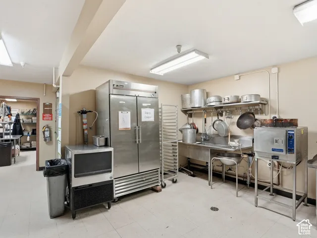 Commercial kitchen featuring stainless steel appliances, stainless steel sink, tile flooring, and fluorescent lighting