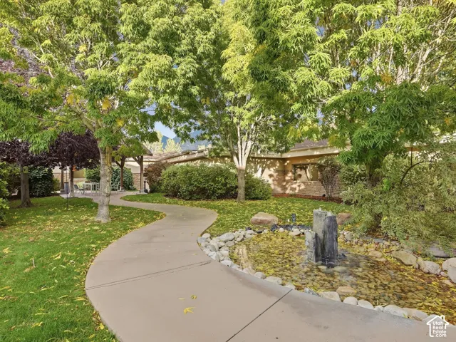 Manicured landscaping with mature trees, a winding concrete pathway, a decorative pond with a stone water feature, and an exterior with stone detailing