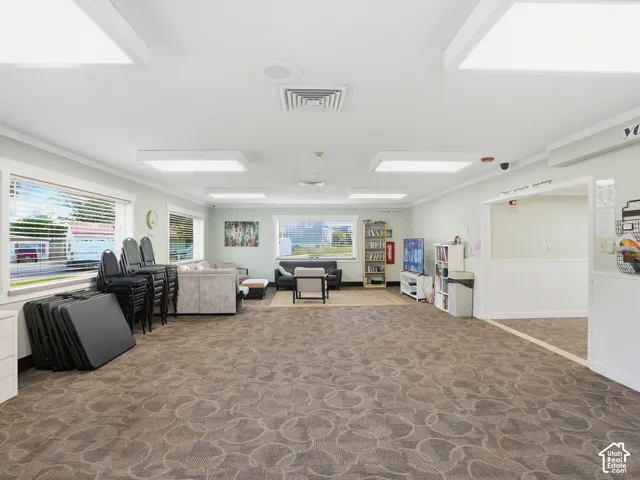 Spacious common area featuring patterned carpeting, multiple windows with blinds, recessed lighting, and an entryway with wainscoting