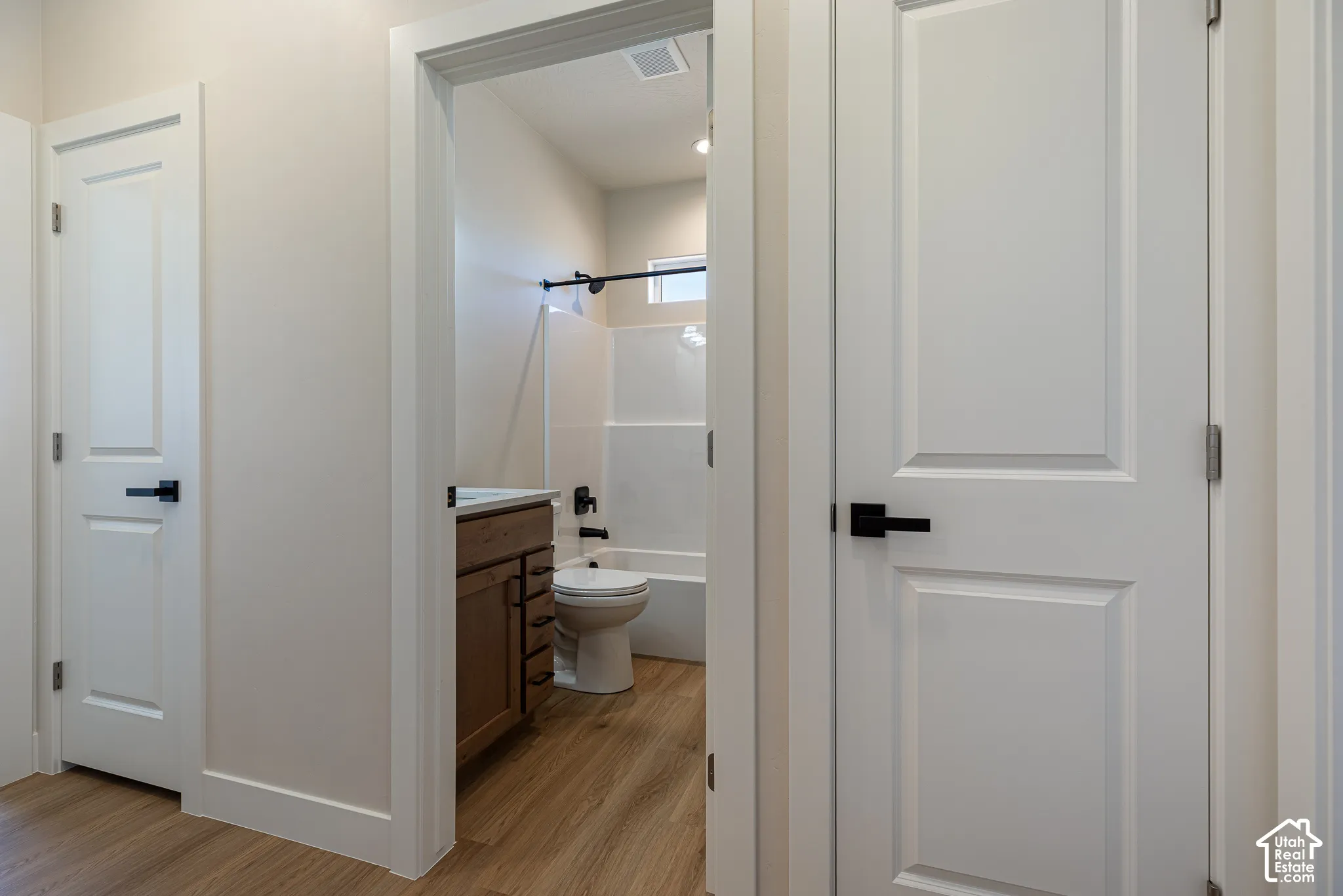 Bathroom featuring a wood-finish vanity with a rectangular sink, a white tub-shower combination, and wood-finish flooring