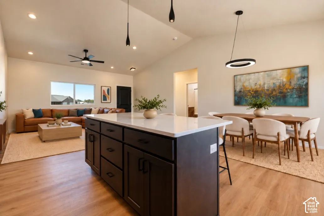 Vaulted ceiling with recessed lighting, wood-finish flooring, kitchen island with a white countertop, large windows, and a ceiling fan