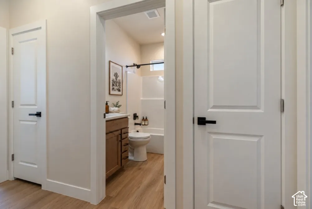 Bathroom with wood-finish flooring, a wood-finish vanity, a white bathtub, and a white toilet