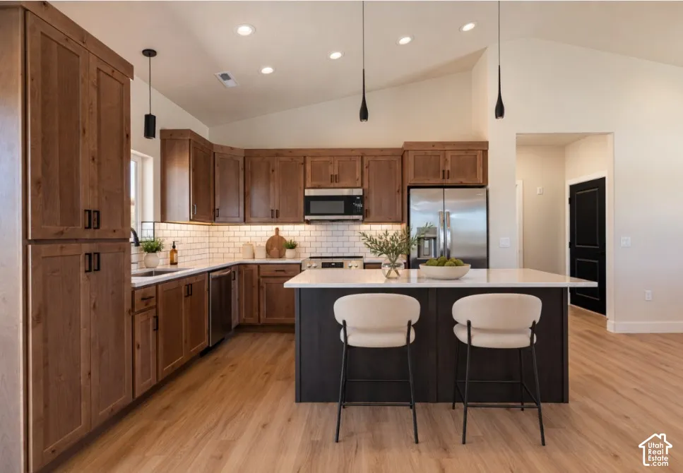 Kitchen featuring wood cabinetry, stainless steel appliances, white subway tile backsplash, and an island with a white countertop