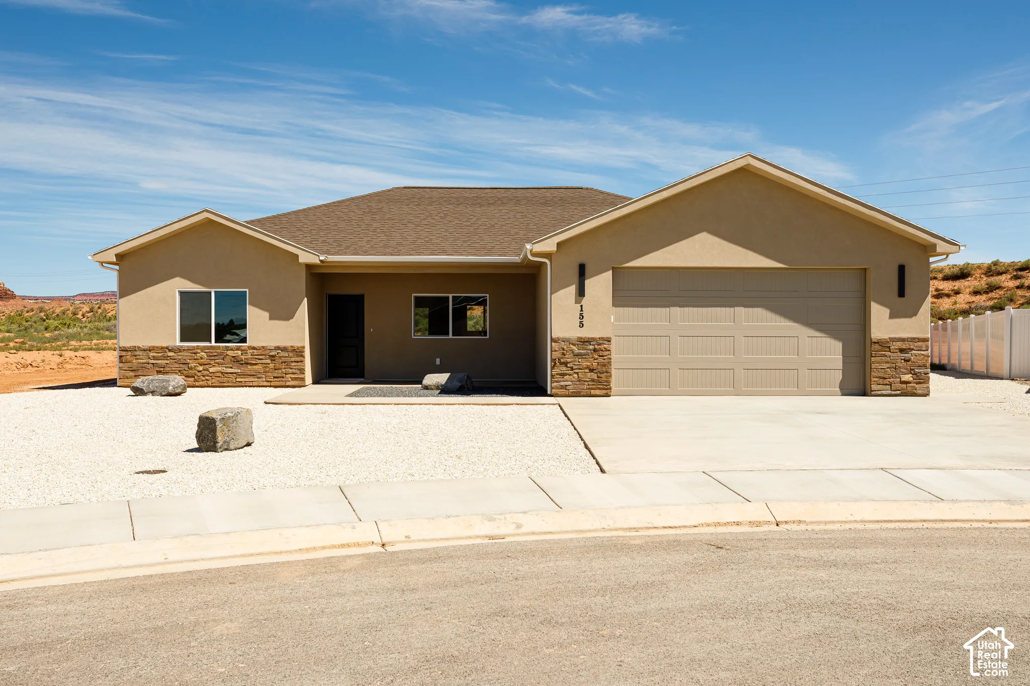 Stucco exterior with stone veneer accents, integrated two-car garage, concrete driveway, and gravel landscaping