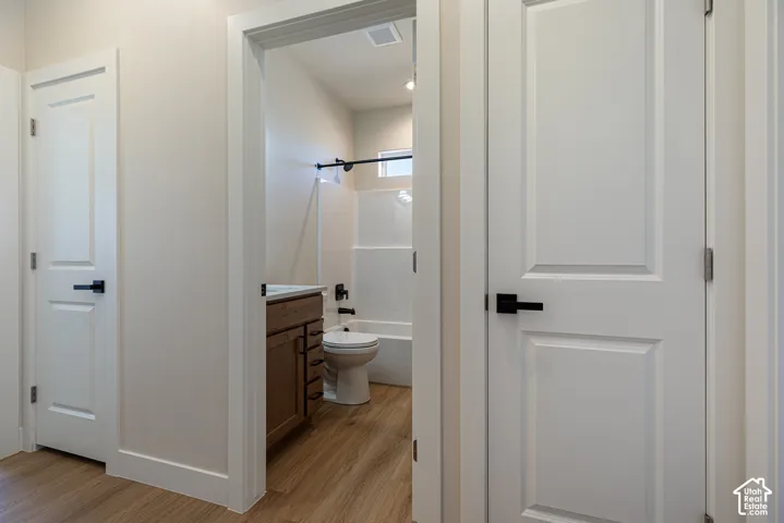Bathroom featuring a wood-finish vanity with a rectangular sink, a white tub-shower combination, and wood-finish flooring