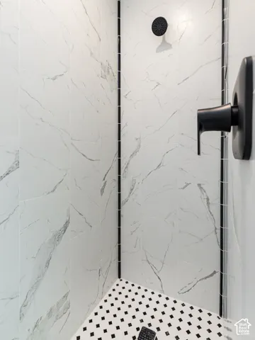 White tile shower with black accent trim, matte black showerhead, matte black shower control, and black and white mosaic tile flooring