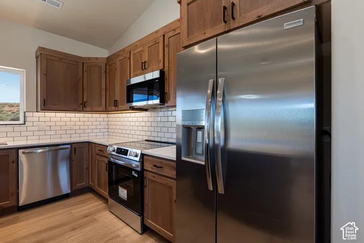 Kitchen featuring wood-finish cabinetry, stainless steel appliances, white subway tile backsplash, and light-colored countertops