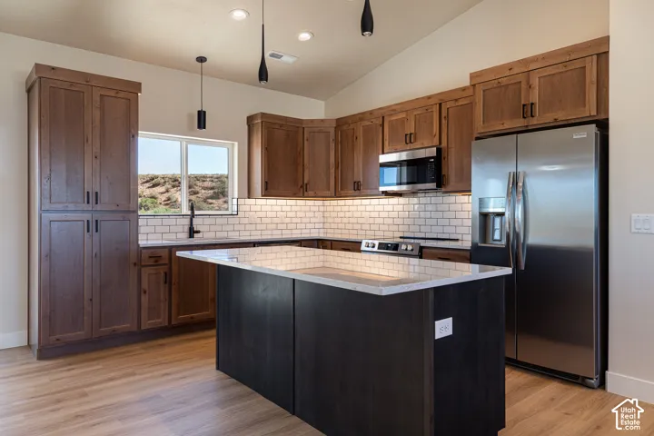 Kitchen featuring wood cabinetry, stainless steel appliances, a center island with a light-toned countertop, subway tile backsplash, and wood-finish flooring