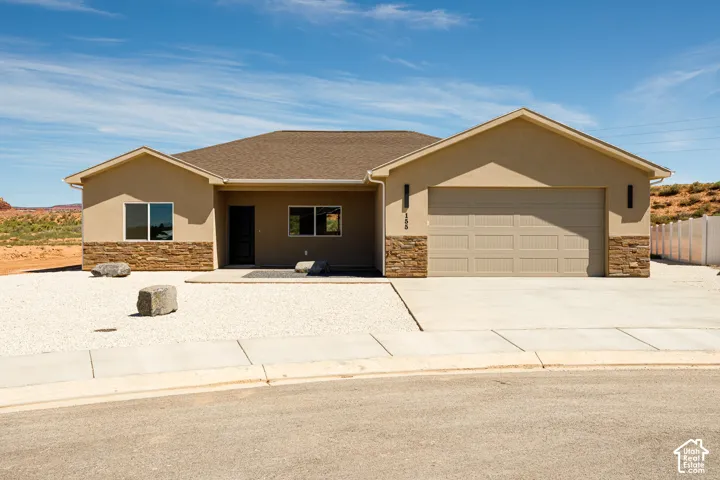 Stucco exterior with stone veneer accents, integrated two-car garage, concrete driveway, and gravel landscaping