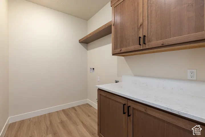 Wood-finish flooring with white baseboards, wood cabinetry featuring black hardware, white countertop, and a wood floating shelf